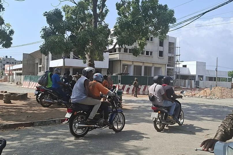 People on motorcycles pass by soldiers guarding a street amid an attempted coup in Cotonou Benin, Sunday Dec. 7, 2025