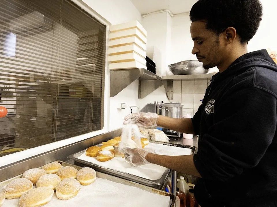 Kidus Michael adds sugar icing to sufganiyot (Hanukkah doughnuts) at Falafel St. Jacques.