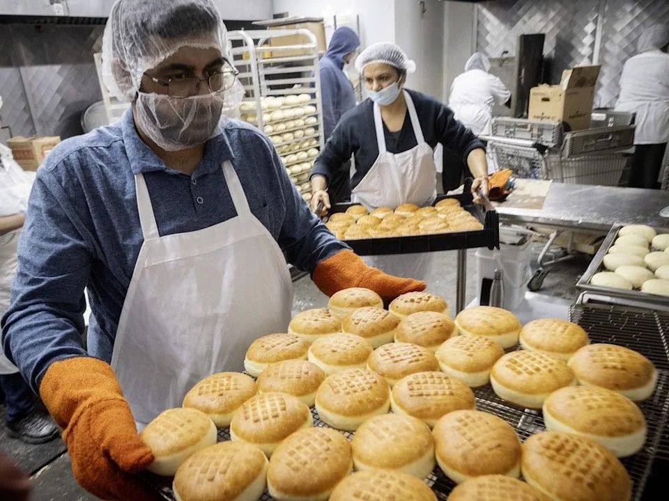 Dharm Sindh, left, handles hot sufganiyot after frying at Montreal Kosher Bakery. Its dough balls are stored on metal screens that go into the fryers so they don’t have to dust with extra flour.