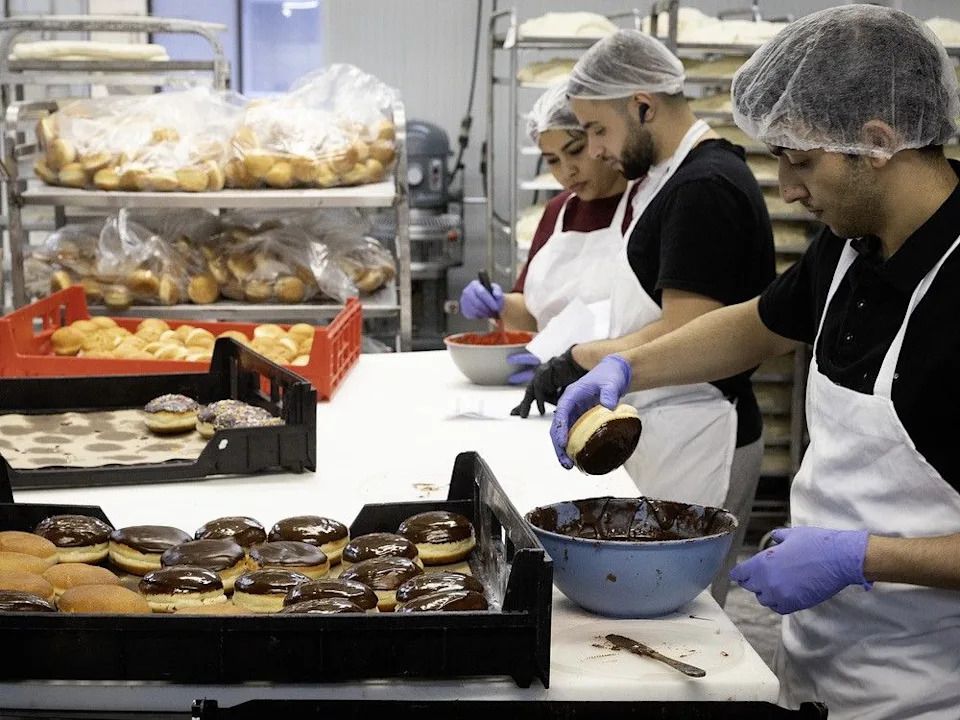 Pouria Karari, front, coats sufganiyot with chocolate at Montreal Kosher Bakery.