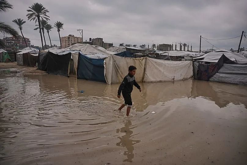 A Palestinian youth walks through a flooded area in a temporary tent camp after heavy rainfall in Deir al-Balah, central Gaza Strip, Friday, Dec. 12, 2025.