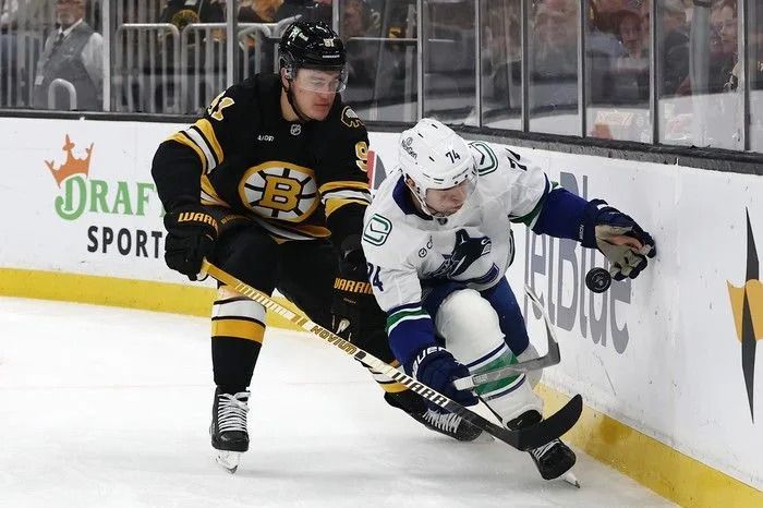Jake DeBrusk of the Vancouver Canucks reaches for a loose puck as Nikita Zadorov of the Boston Bruins tries to ride him into the boards during the second period at TD Garden on Dec. 20, 2025 in Boston.