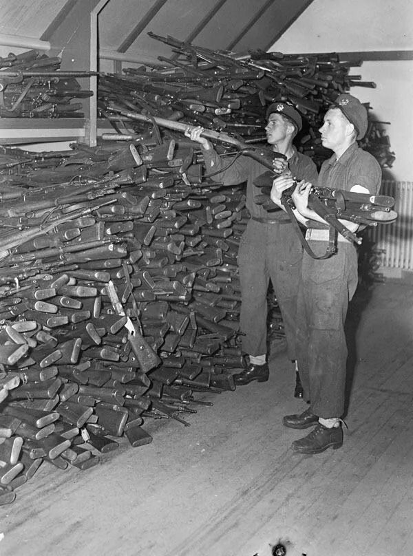 Privates J.A. Taylor and J.D. Villeneuve of the Royal Canadian Regiment stacking rifles turned in by surrendering German soldiers, IJmuiden, Netherlands on May 11, 1945.