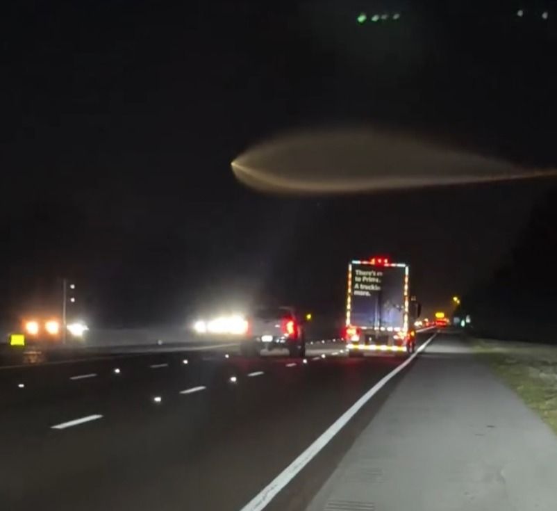 A video still of an unidentified flying object in the night sky above a highway.